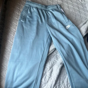 Blå mjukisbyxor från Nike - Säljer ett par bekväma blå mjukisbyxor från Nike med elastisk midja och sidofickor. Perfekta för en avslappnad stil. Nike-loggan syns tydligt på benet. Storlek 147-158 cm  från barnavdelningen
