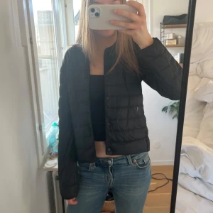 Svart dunjacka från Uniqlo - Säljer en svart, lätt och smidig dunjacka från Uniqlo. Jackan har en minimalistisk design med knappar framtill och är perfekt för lager-på-lager. Den är långärmad och har en rund halsringning. Perfekt för kyliga dagar när du vill hålla det enkelt och stilrent. 