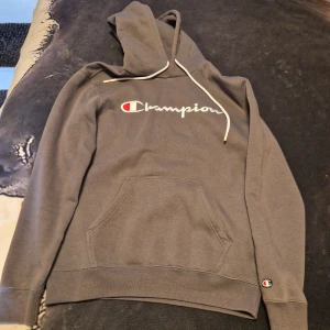 Svart hoodie från Nike - Säljer en svart hoodie från Nike med stor logga och text i gult och grått. Tröjan har en klassisk känguruficka och justerbar huva med snören. Perfekt för en sportig look eller avslappnad stil.