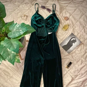 Mörkgrön sammets jumpsuit  - Snygg mörkgrön jumpsuit i sammet med smala axelband och knytning framtill. Den har en elegant omlott-design och en smickrande passform. Perfekt för en kväll ute eller en speciell tillställning. Pris går att diskuteras! 