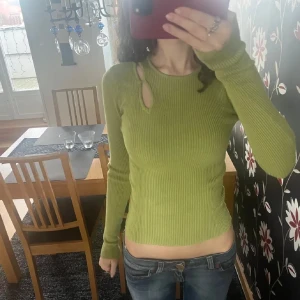 Grön tröja med cut-out detaljer - Snygg grön ribbad tröja med unika cut-out detaljer vid axeln. Tröjan har en tight passform och långa ärmar, perfekt för en trendig look. Har en liten defekt vid cutout detaljen då det är en liten grej som lossnat där, skriv privat för bilder på det💛