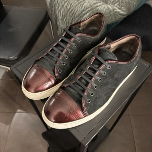  Lanvin - Snygga svarta sneakers från Lanvin med vinröda detaljer och snörning. Skorna har en vit sula och en glansig vinröd tåhätta som ger en unik look. Perfekta för att lyfta din stil.