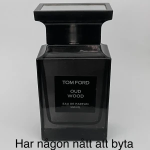 Tom Ford Oud Wood Eau de Parfum 100 ml - Säljer en exklusiv Tom Ford Oud Wood Eau de Parfum i en elegant mörk flaska på 100 ml. Doften är känd för sina rika och träiga noter, perfekt för den som vill ha något unikt och sofistikerat. Flaskan har en stilren design med en fyrkantig form och ett matchande lock.
