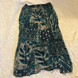 Mönstrad kjol från Zara - Snygg mönstrad kjol från Zara i gröna och blå toner. Kjolen har ett unikt mönster med inslag av olika former och färger. Perfekt för dig som vill ha något annorlunda i garderoben. Tillverkad i ett lätt och luftigt material. Ena snöret är lite sönder (bild 4)