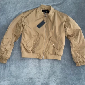 Bomberjacka  - Säljer en snygg beige bomberjacka från Vero Moda. Jackan har en dragkedja framtill och ribbade muddar vid ärmslut och nederkant. Perfekt för en stilren look och våren. Helt ny med prislapp kvar.