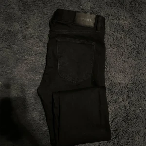  J.Lindeberg svarta jeans - Snygga svarta jeansbyxor från J.Lindeberg med klassisk femficksdesign. Byxorna har en knappgylf. Passar bra till både vardag och mer uppklädda tillfällen.