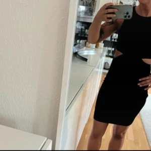 Svart klänning med cut-out detaljer - Snygg svart klänning med cut-out detaljer i midjan. Perfekt för en kväll ute eller en speciell tillställning. Klänningen är tight och kort, vilket ger en stilren och modern look. Aldrig använd 