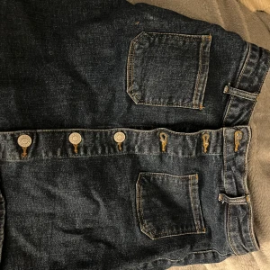 Mörkblå jeansshorts med knappar - Snygga mörkblå jeansshorts med framträdande knappar och praktiska fickor. Perfekta för en avslappnad stil. Passar bra till både t-shirt och skjorta.