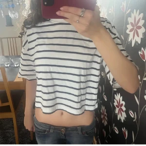 Randig tröja - Säljer en vit och svart randig t-shirt med korta ärmar. Den har en avslappnad passform och är perfekt för en casual look. Passar bra till jeans eller shorts.