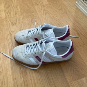 Adidas Gazelle sneakers i beige och vinröd - Skicket syns på bilderna. Snygga Adidas Gazelle sneakers i beige mocka med vinröda och vita detaljer. 