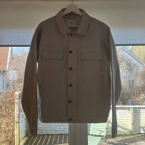 Beige överskjorta från Woodbird - Säljer en stilren beige jacka från Woodbird i storlek M. Jackan har knappar framtill och två bröstfickor. Tillverkad i 100% bomull. Perfekt för vår och höst! Hör av dig om du vill ha fler bilder. 🙌🏻 Nypris 1199kr.