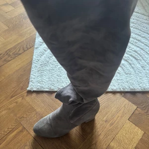 Grå stövlar i mocka - Snygga grå stövlar i mocka med en stilren design. Perfekta för att ge en elegant touch till din outfit. De är knähöga och har en mjuk finish.