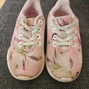 Rosa blommiga sneakers - Säljer ett par söta rosa sneakers med blommigt mönster. Skorna har snörning och en bekväm vit sula. Perfekta för en avslappnad stil med en touch av färg och mönster.