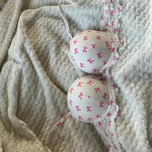 Vit och rosa bh rosa rosetter på den. De är push och de är spets på den. Den är använd en gång bara för den var för liten för mig. - Säljer en söt vit bh från NEW YORKER  med rosa rosett-mönster och spetsdetaljer. Bh:n har en liten silverfärgad rosett mellan kuporna och justerbara axelband. Perfekt för dig som gillar en mjuk och fin bh den är skön och mjuk. Inte satt pris kom med förslag på pris.
