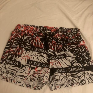 Mönstrade shorts från Dolce & Gabbana - Snygga shorts från Dolce & Gabbana med ett tropiskt mönster i svart, vitt och rött. De har en elastisk midja och snörning för justerbar passform. Perfekta för en avslappnad stil med en lyxig touch.