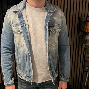 Blå jeansjacka från Calvin Klein jeans - Säljer en klassisk blå jeansjacka med knappar framtill och två bröstfickor med lock. Jackan har en snygg tvättad look och långa ärmar. Perfekt för en avslappnad stil. Storlek M