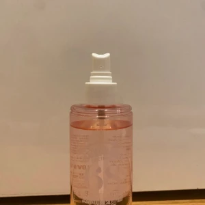 Parfymmist med vit kork - En fräsch parfymmist i en genomskinlig flaska med rosa vätska. Flaskan har en vit spraykork och ett elegant vitt lock med upphöjd text. Perfekt för en snabb uppfräschning under dagen.