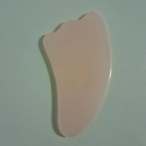Rosenkvarts gua sha-sten - Säljer en rosa gua sha-sten för ansiktsmassage. Den har en mjuk, böjd form som är perfekt för att massera och stimulera huden. Perfekt för daglig hudvårdsrutin.