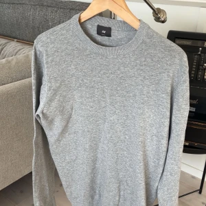 Grå tröja från H&M - Säljer en stilren grå tröja från H&M. Den har en klassisk rund hals och långa ärmar, perfekt för en avslappnad look. Tröjan är tillverkad i ett mjukt material som känns skönt mot huden.