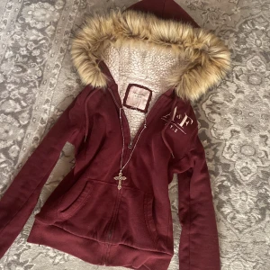 Vinröd hoodie från Abercrombie & Fitch - Säljer en vinröd hoodie från Abercrombie & Fitch med fuskpälsfodrad huva och dragkedja. Storlek S. 🎀
