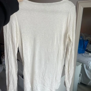 Vit långärmad tröja - En enkel och stilren vit långärmad tröja i tunt material. Perfekt att ha som basplagg eller under en kofta. Tröjan har rund halsringning och rak passform.