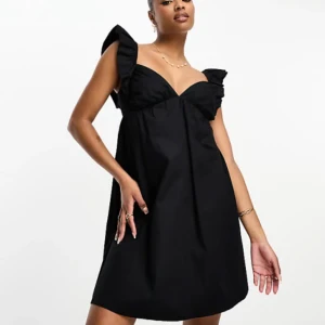 Svart klänning med volangaxelband - Supersöt svart klänning med volangprydda axelband och lätt v-ringad byst. Klänningen har en luftig passform och är perfekt för dig som gillar en stilren look med en twist. Materialet känns mjukt och följsamt.