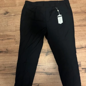 NYA Svarta croppade kostymbyxor från These Glory Days - Säljer ett par svarta croppade kostymbyxor från These Glory Days. Byxorna har slim fit-passform och klassisk design med hällor för bälte. Perfekta för en stilren look.