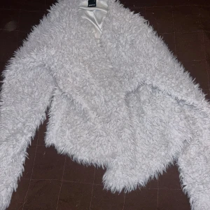 Vit fluffig jacka från Gina Tricot - Säljer en supermjuk och fluffig vit jacka från Gina Tricot. Jackan har lång ärm och är täckt av pälsliknande material som ger en cool och trendig look. Perfekt för dig som vill sticka ut lite extra!
