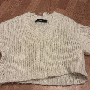 Vit stickad croppad tröja från Vero Moda - Mysig vit stickad tröja från Vero Moda med v-ringning och croppad passform. Tröjan har långa ärmar och ribbade muddar vid hals, ärmslut och nederkant. Perfekt för lager-på-lager-stil.