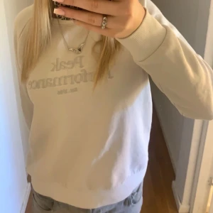 Beige sweatshirt från Peak Performance - Säljer en beige sweatshirt från Peak Performance med broderad logga framtill. Tröjan har rund halsringning och långa ärmar med ribbade muddar. Perfekt för en avslappnad stil.
