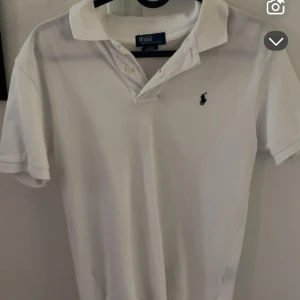 Vit pikétröja från Polo Ralph Lauren - Klassisk vit pikétröja från Polo Ralph Lauren med kort ärm och broderad logga på bröstet. Perfekt till jeans eller shorts för en stilren look.
