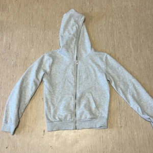 Ljusgrå lager 157 hoodie med dragkedja - Säljer en enkel och stilren ljusgrå hoodie med dragkedja framtill och två fickor. Perfekt för chill dagar eller när du vill ha något bekvämt. Huva och långa ärmar ger extra mysfaktor. Från lager 157
