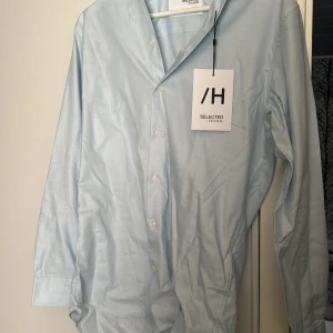 Ljusblå skjorta från Selected Homme - Säljer en klassisk ljusblå skjorta från Selected Homme i storlek XS. Skjortan har lång ärm, knappar framtill och en stilren, tidlös design. Perfekt för dig som gillar en enkel och snygg look.