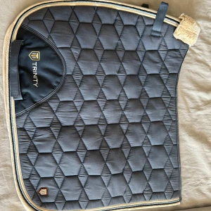 Trinity shabrak - Helt nytt dressyrshabrak från Trinity. Använt max 2 gånger och helt rent (även tvättat).❤️ Ligger fint och stilla på hästryggen. Nypris: 500 Säljes för: 250. Priset kan diskuteras!