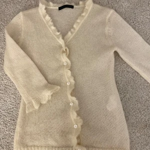 Ljusgul kofta med volangkant - Jättesöt ljusgul stickad kofta med volangdetaljer längs knäppningen och vid ärmsluten. Den är tunt stickat och lite genomskinlig men är perfekt att slänga över ett linne för en söt och härlig look. Köpte utomlands så vet inte märket men är i bra skick och har bara använt en gång. Står inte storlek men skulle säga att det är en s 💕