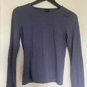 Blå långärmad topp från Gina Tricot - En enkel och stilren blålilagrå långärmad topp från Gina Tricot. Modellen har rund halsringning och är tillverkad i ett mjukt bomullsmaterial. Perfekt att matcha med jeans eller kjol för en clean look. Skriv gärna prisförslag! 