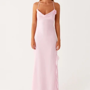 Ljusrosa långklänning med rosdetalj - Säljer en jättefin slutsåld ljusrosa klänning🩷 Klänningen har öppen rygg med korsade band och en slits med volangdetalj längs sidan. Perfekt för bal eller festliga tillfällen, är ej använd bara testad💗