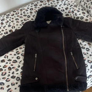 Svart fodrad jacka med dragkedja - Säljer en svart jacka från Stradivarius i strl S med mjukt svart foder. Jackan har dragkedja framtill, två fickor med dragkedja och dekorativa spännen vid midjan. Perfekt för kyliga höst men också vinter dagar