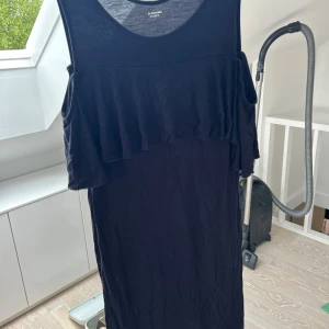 Svart klänning med volang från Calzedonia - Svart ärmlös klänning från Calzedonia med volangdetalj över bröstet. Enkel och stilren design i mjukt material, perfekt för varma dagar eller att styla upp med accessoarer.