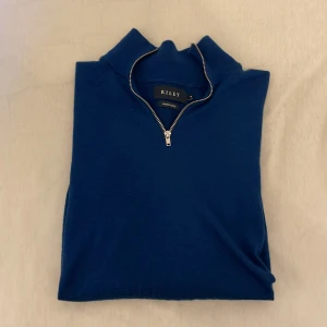 Mörkblå halvzip-tröja från Riley - Säljer en stilren mörkblå långärmad tröja från Riley med halv dragkedja i halsen. Tröjan har en klassisk passform och är perfekt för lager-på-lager. Materialet känns mjukt och bekvämt.