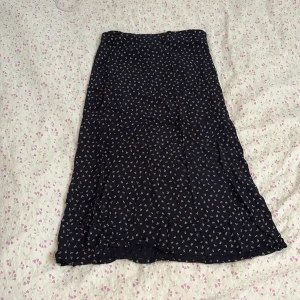 Brandy Melville kjol  - Svart kjol med små vita mönster, lätt utsvängd modell och mjukt fall. Perfekt för dig som gillar en enkel men ändå söt stil. Kjolen har en bekväm midja och är i en längre längd.