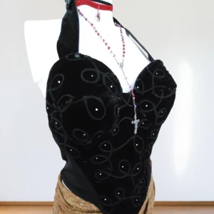 Sällsynt Vintage Sammetkorsett från COCO – Gotisk Romantik / Dark Academia / Fairycore – Stl M  - Storlek: M / 38–40 / UK 10–12     • Märke: COCO (Vintage 80-tal)     • Skick: Vintage – mycket fint skick     • Material: Lyxig svart sammet med broderi och pärldetaljer     • Stängning: Dragkedja bak     • Färg: Djupsvart      • Matcha med en lång spetskjol och kängor för en gotisk look     • Bär över en vit blus och plisserad kjol för romantisk akademisk stil     • Kombinera med flytande tyger och naturinspirerade accessoarer för en fairycore-outfit