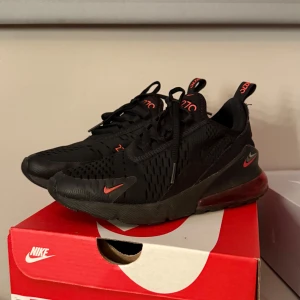 Nike Air Max 270 Svarta Sneakers - Säljer ett par svarta Nike Air Max 270 sneakers med röda detaljer. Riktigt sköna använda men i väldigt fint skick en liten repa eller vad man ska säga på vänser häl. Skriv för frågor eller prisförslag 💞