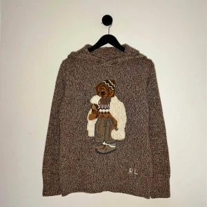 Ralph lauren polo bear knit hoodie - Säljer en brunmelerad stickad hoodie från Ralph Lauren med ett stort broderat björnmotiv på framsidan. Tröjan har huva och långa ärmar, perfekt för en avslappnad och trendig stil. Kvitto finns och du kan se det på sista bilden. Ny pris ligger på ungefär 6 tusen.