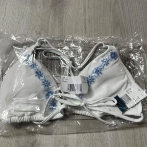 Vit bikiniöverdel med blå broderade blommor - Vit triangelbikini med blå broderade blommor från Hollister. Säljer pga råkade beställa två likadana. Har fått otroligt mycket komplimanger för den, supersöt💫
