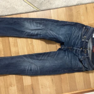 Mörkblå jeansbyxor från Seven7 - Säljer ett par mörkblå jeansbyxor från Seven7 med klassisk femficksdesign och orangea kontrastsömmar. Jeansen har normal passform och raka ben, perfekt för en avslappnad stil. Snygga slitningar framtill för en trendig look.