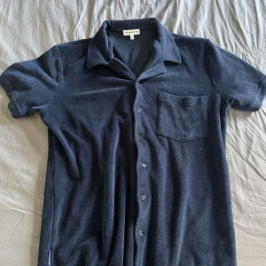 Mörkblå piquéskjorta från The Resort Co - Säljer en mörkblå kortärmad piquéskjorta från The Resort Co i storlek M.  Skick 8/10 Skjortan har klassisk krage, bröstficka och knappar framtill. Perfekt för en avslappnad och stilren look. Materialet är mjukt och andas bra.