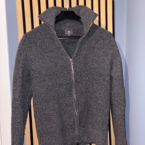 Grå stickad kofta med dragkedja från H&M - Säljer en stilren grå stickad kofta från H&M med hel dragkedja framtill och hög krage. Perfekt för lager-på-lager och passar till många olika outfits. Klassisk och enkel design. Storlek: m/l men passar konstigt nog S