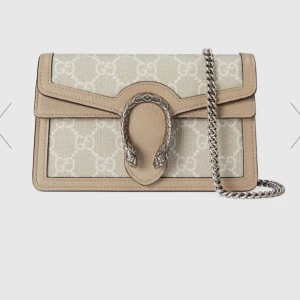 Beige axelväska från Gucci med kedja - Säljer en beige axelväska från Gucci med klassiskt GG-mönster och snygga skinn-detaljer. Väskan har en silverfärgad kedja och ett dekorativt spänne framtill. Perfekt för dig som vill ha en stilren och lyxig accessoar. Pris kan diskuteras. Använt ett par gånger bara