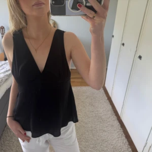 Svart v-ringad topp från Gina Tricot - Säljer en svart v-ringad topp från Gina Tricot i storlek 38. Toppen är ärmlös med öppen rygg och knytband bak. Perfekt för varma dagar och enkel att styla till olika outfits.